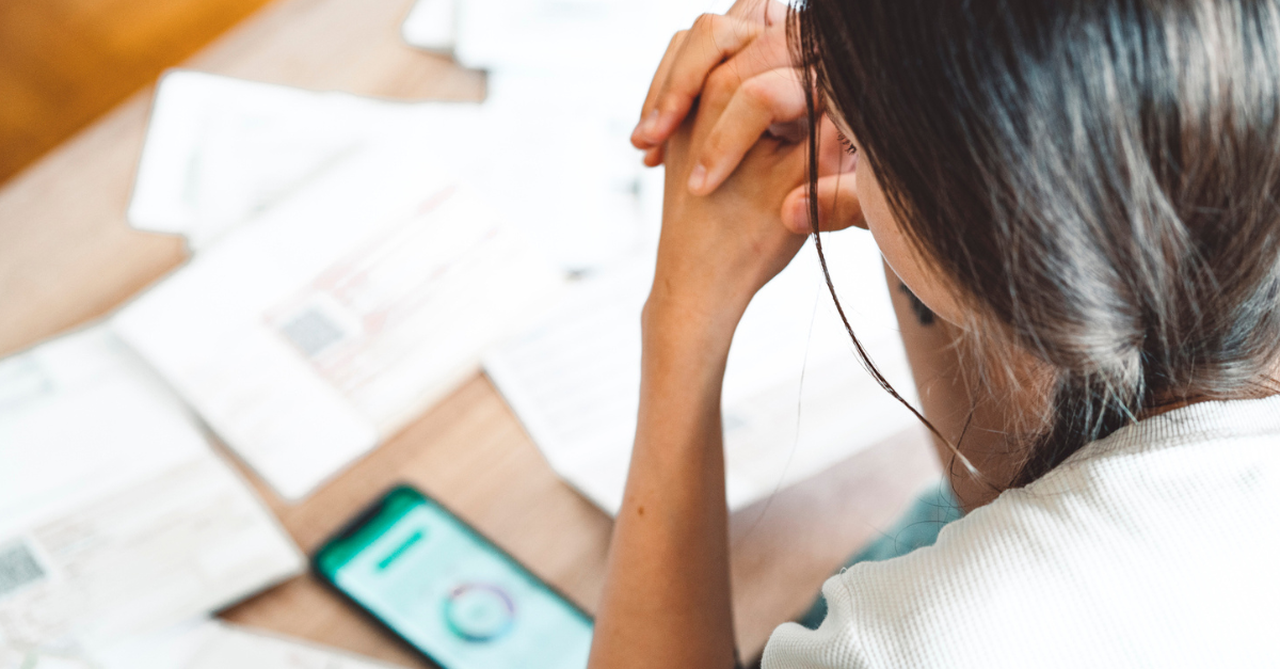 Woman stressed about finances, hands on her head looking at bills.