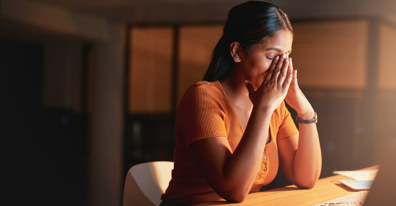 Emotional woman sitting at her desk with her head in her hands.