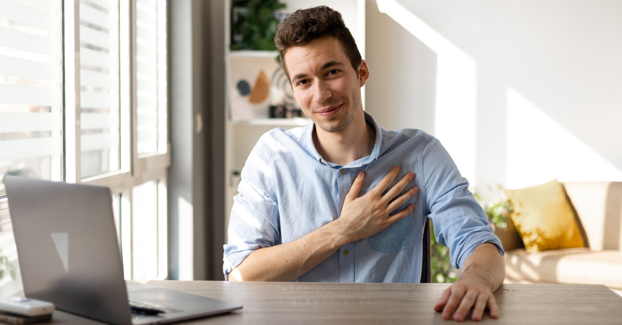 Grateful man with hand on his heart sitting at his desk in front of a computer.