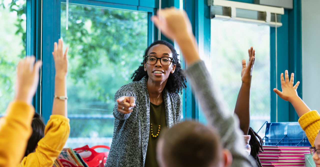 Teacher in her classroom, children with hands raised