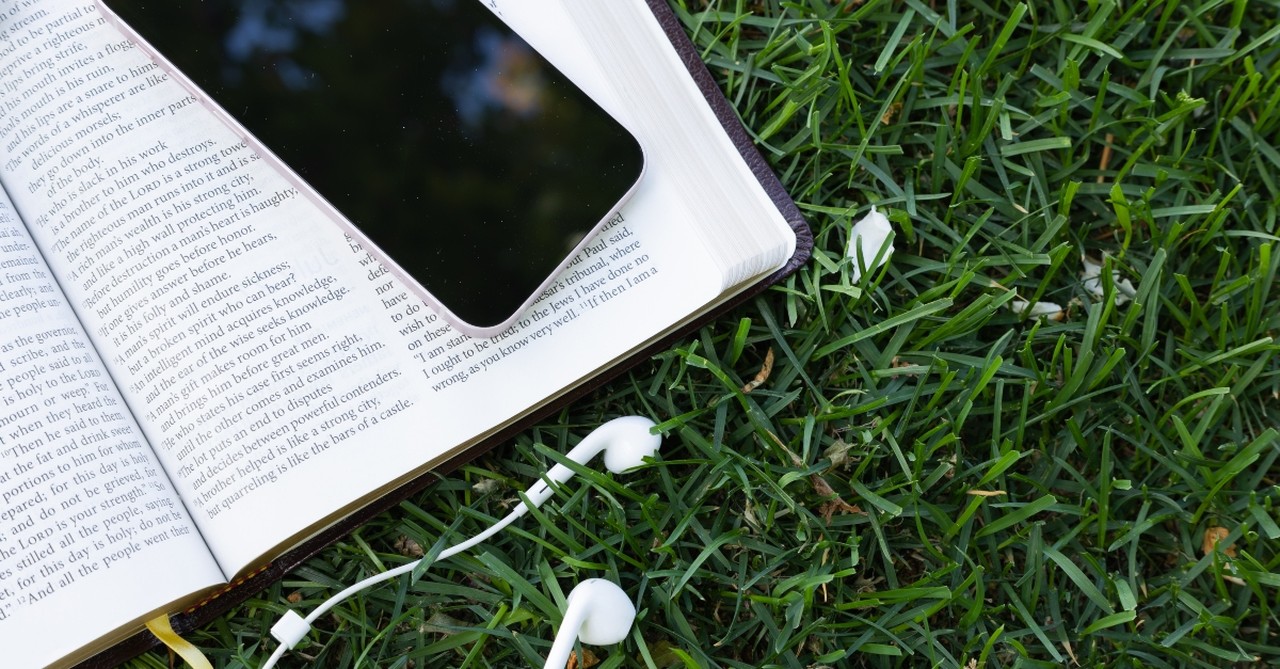 Bible and phone with headphones outside in the grass