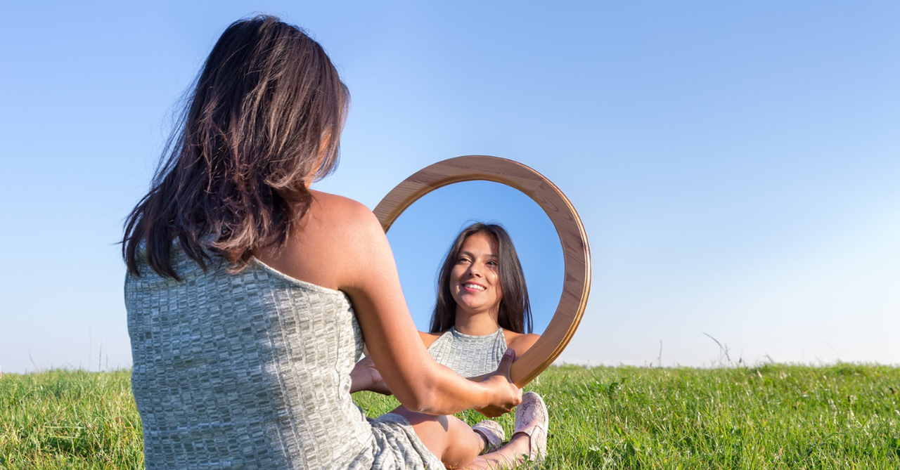 Woman sitting outside, looking in a small mirror; the world's standards are a dangerous distraction from beauty in Christ.