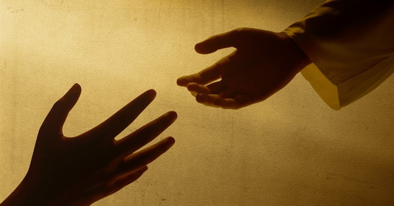 Silhouette of one hand reaching out to another for help