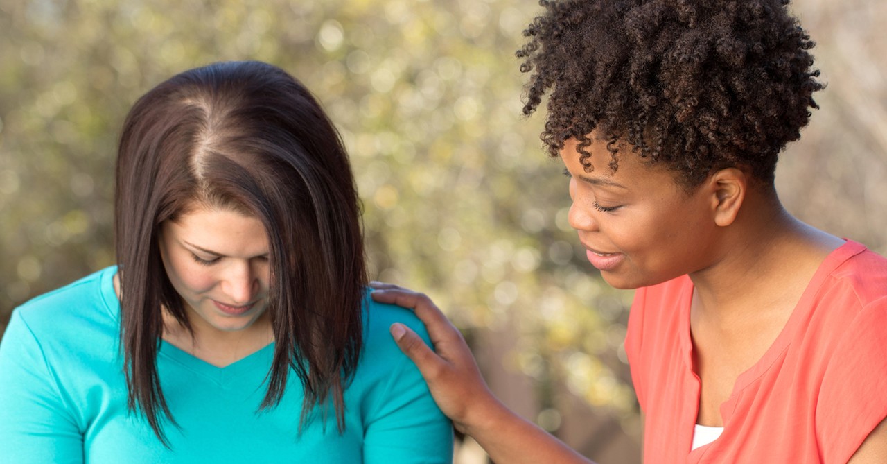 one woman praying for another woman outside at table