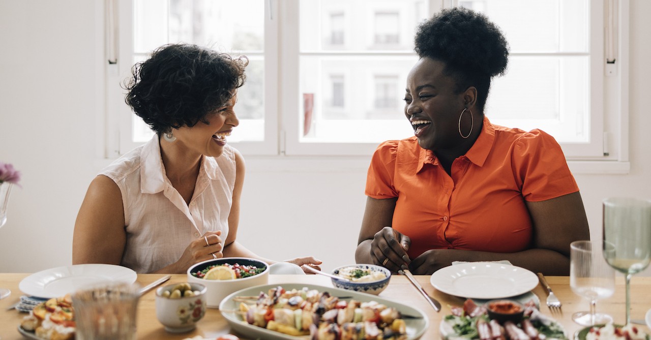 happy women friends laughing and eating dinner at home