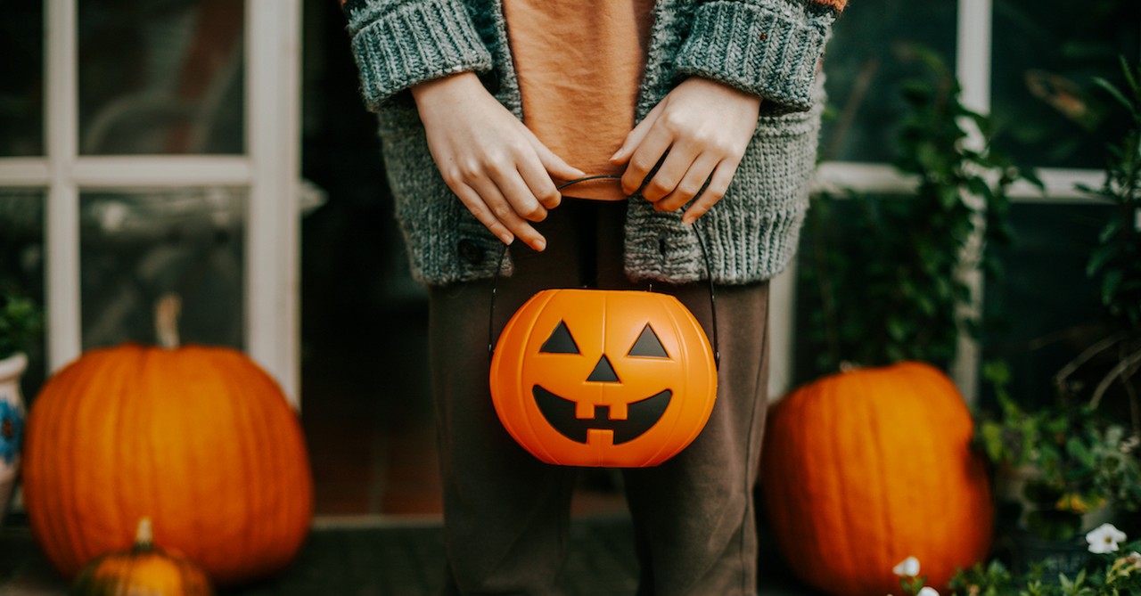 person holding halloween trick or treat pumpkin bucket on front porch