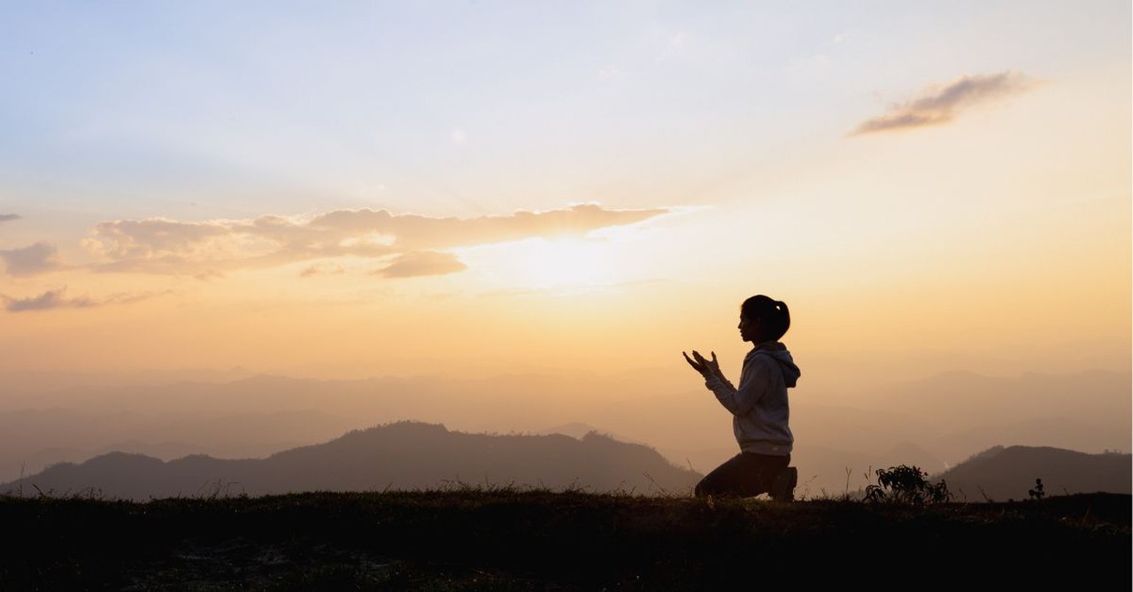 A woman praying outside at sunrise