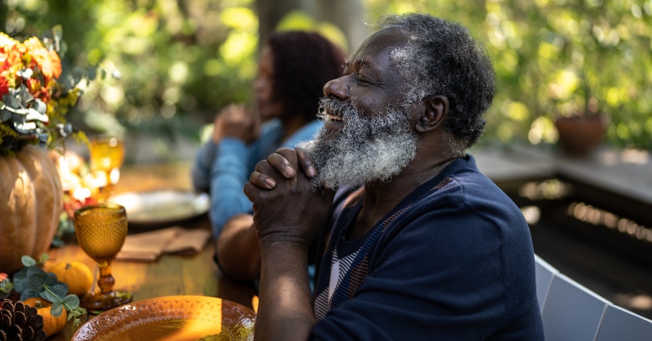 Senior man joyfully praying at Thanksgiving dinner