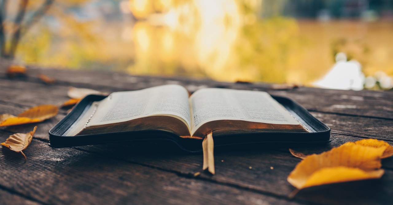 Bible laying open on table outside during autumn day with leaves