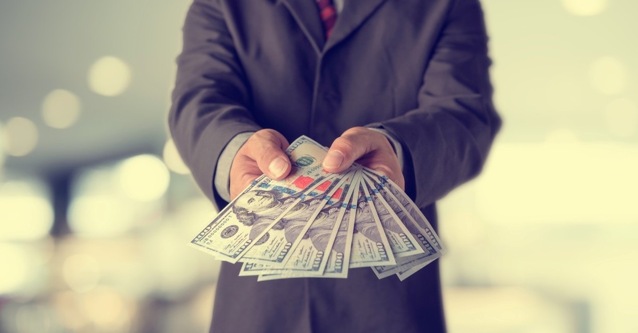 businessman holding out hundred dollar bills to illustrate what the bible says about managing money wisely