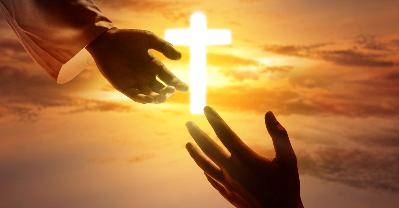 jesus hand reaching out to human's hand with cross in background