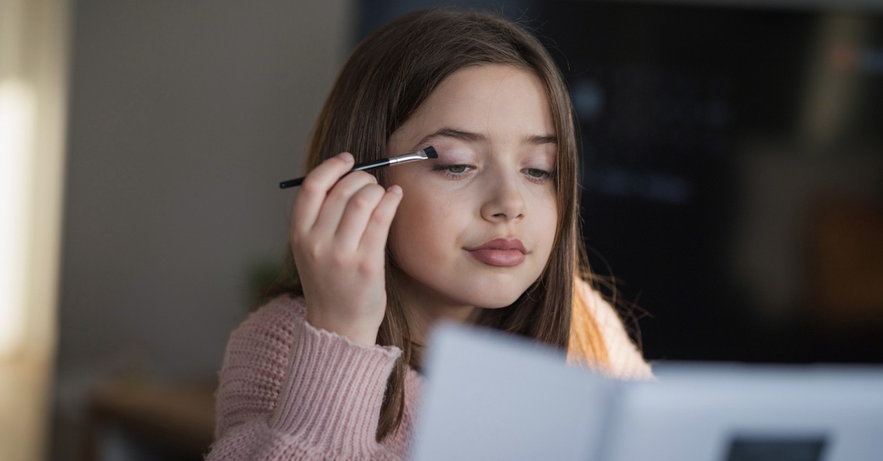 Young girl teen putting on makeup in mirror