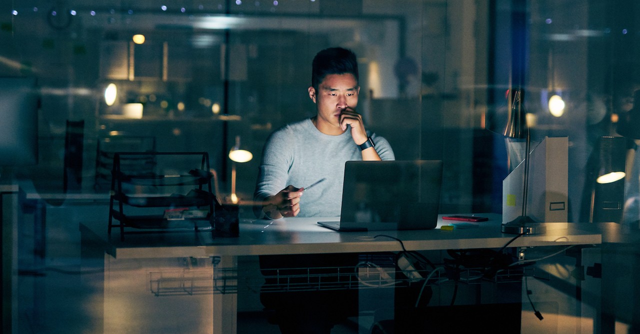 Asian man working late on laptop at office job workaholic