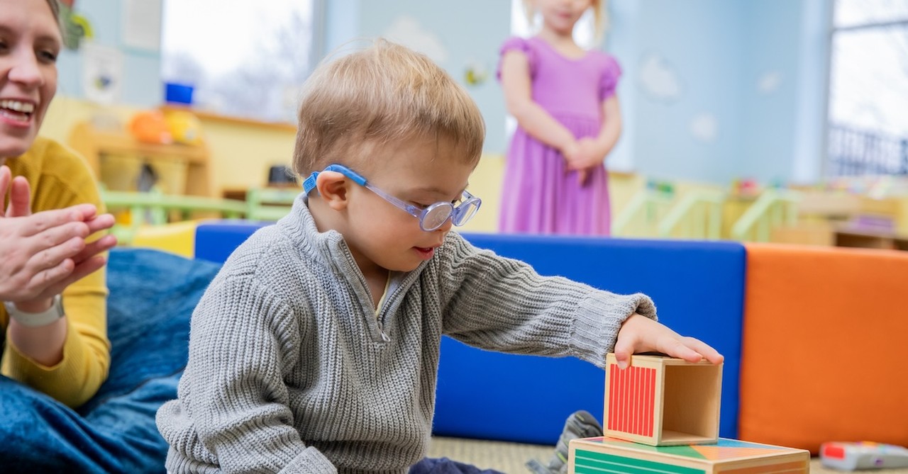 Little boy with Down Sydrome disability playing with toys teacher