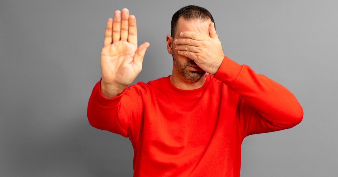 man covering his eyes and holding up a hand to illustrate ignoring someone, warning signs of a narcissistic pastor