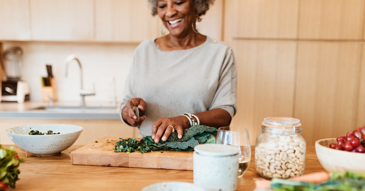 Happy senior woman cooking salad in kitchen