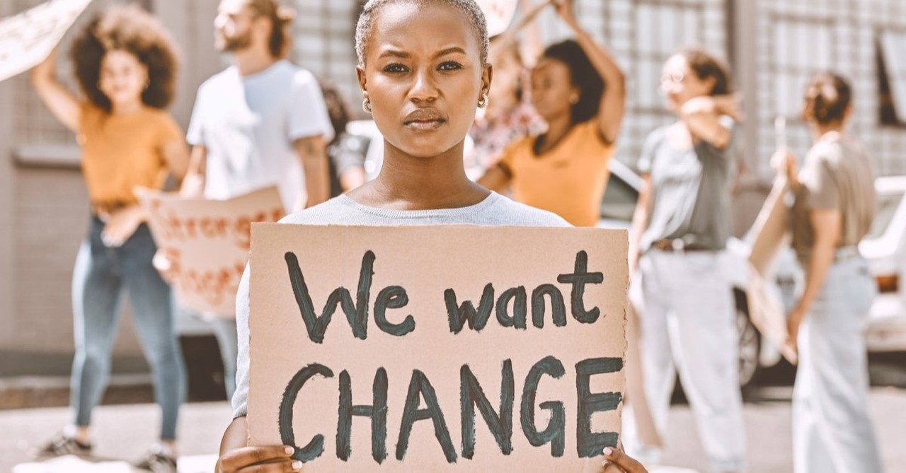 woman holding protest sign that says we want change, reasons that women are vital to the church community