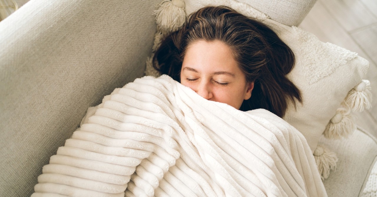 Happy, relaxed woman snuggled up under a fluffy blanket