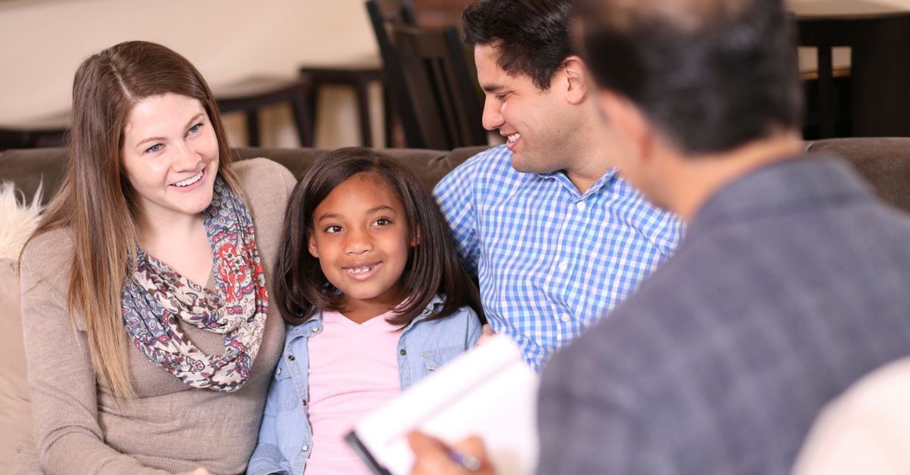 A young girl sitting with two adults, completing adoption process