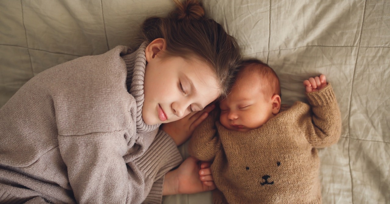 Big sister cuddled up with baby brother, taking a nap