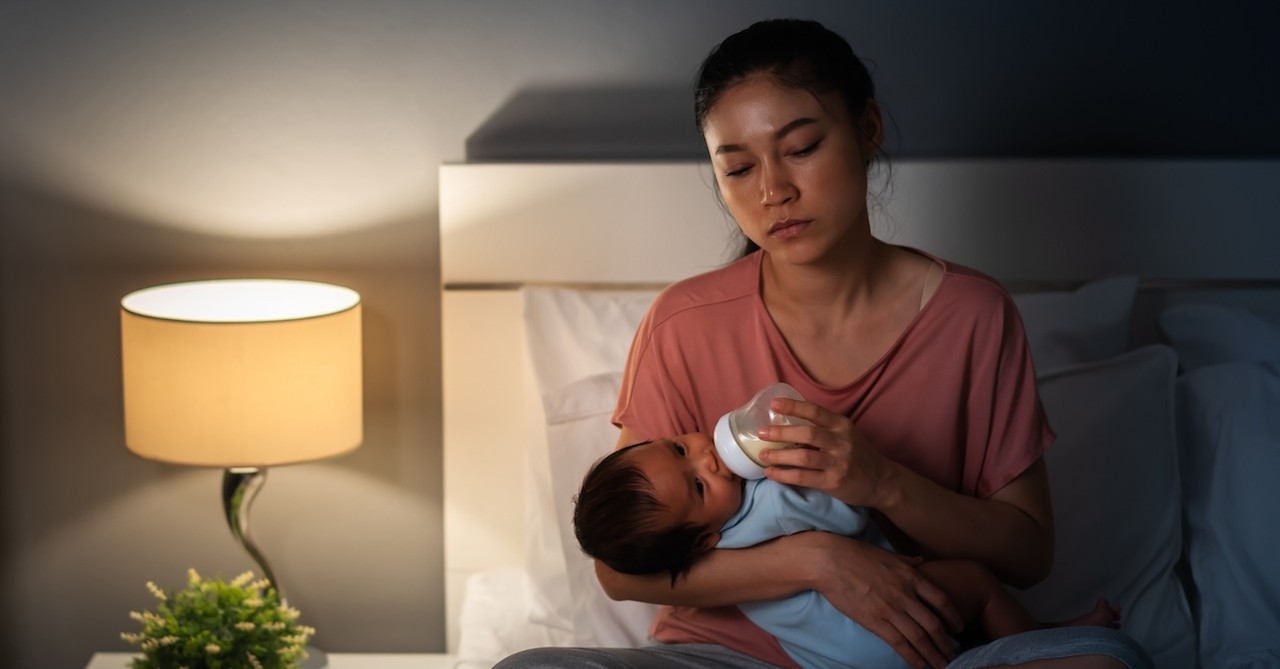 Exhausted tired mom late night feeding newborn baby in bed