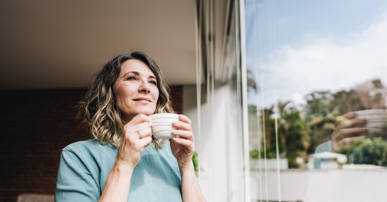 smiling woman drinking coffee in the morning looking out window