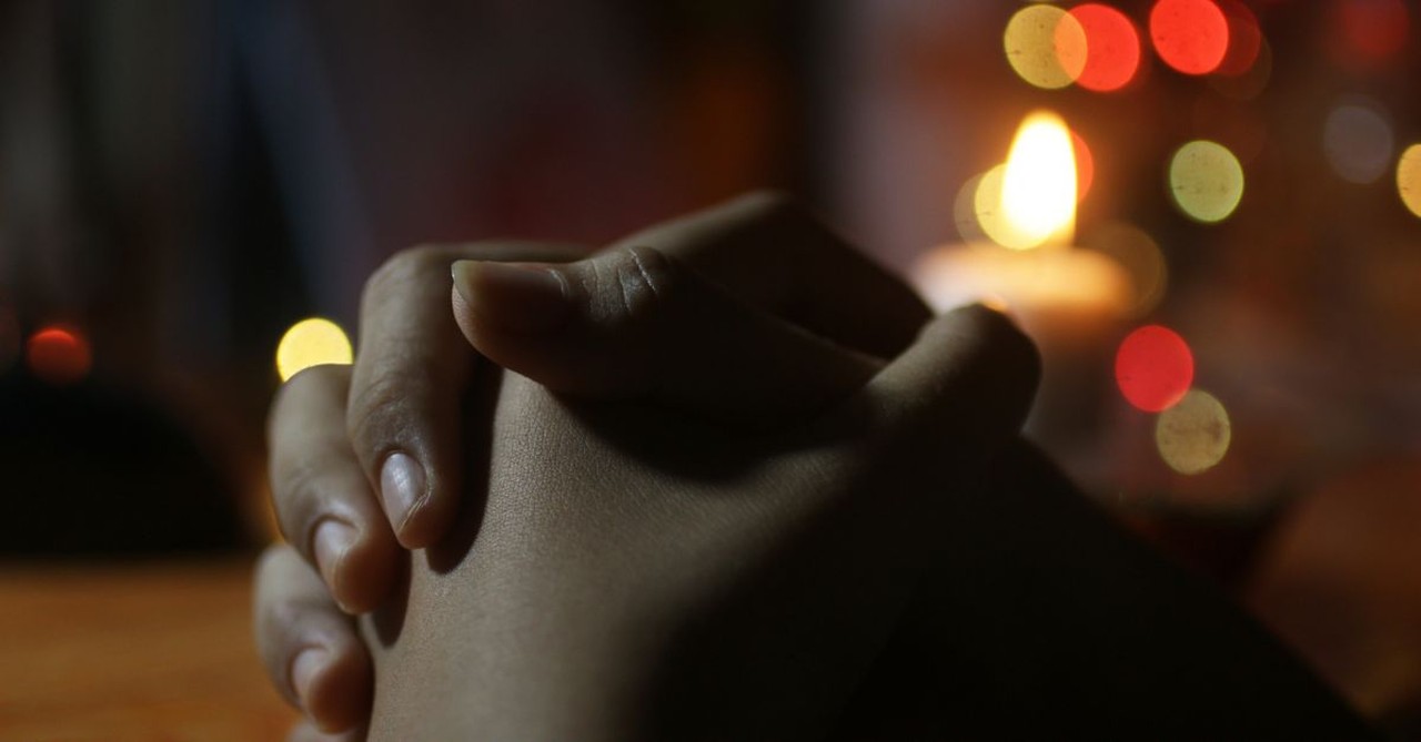 Praying hands with Christmas lights in the background; prayers for Advent