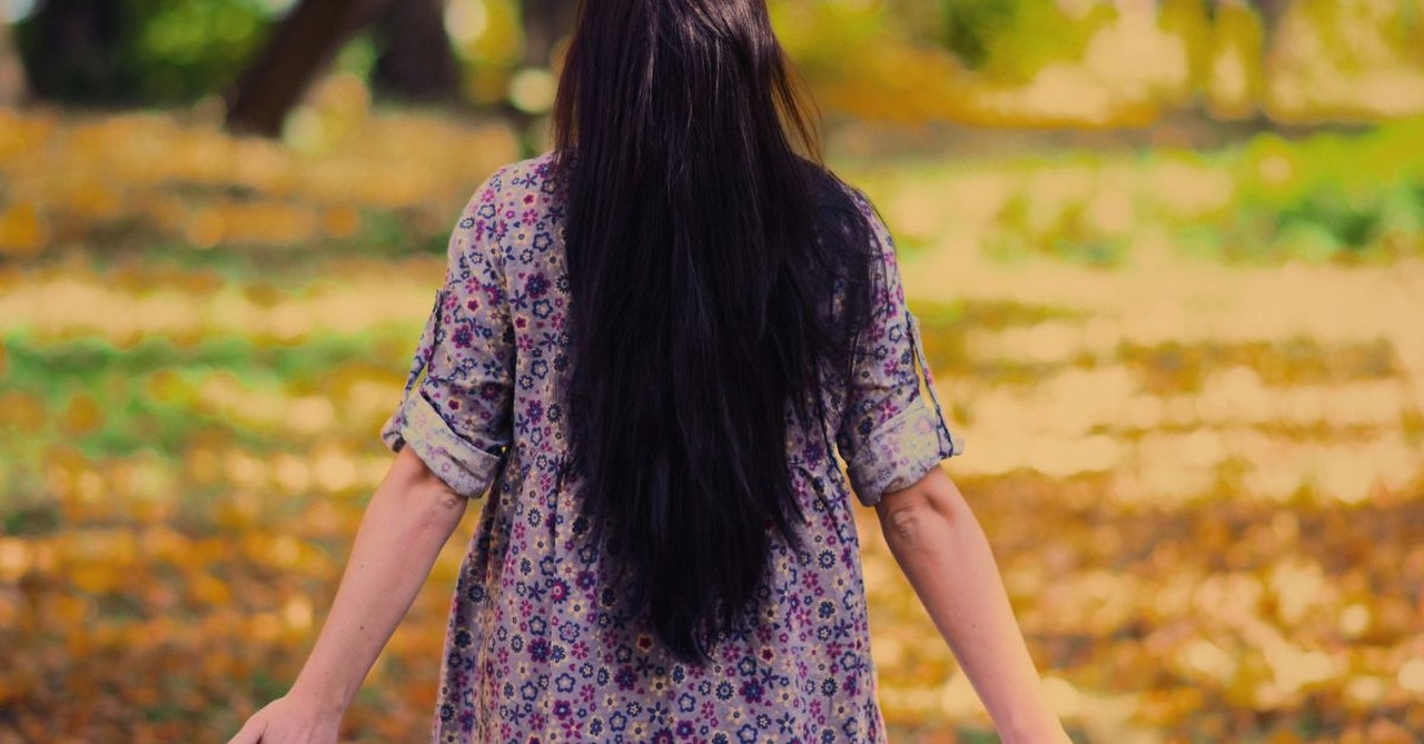 Woman walking in the woods in the fall; what do you need to let go of in order to grow?