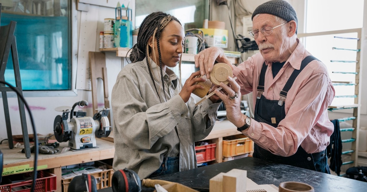 A senior man helping a young woman with a woodworking project