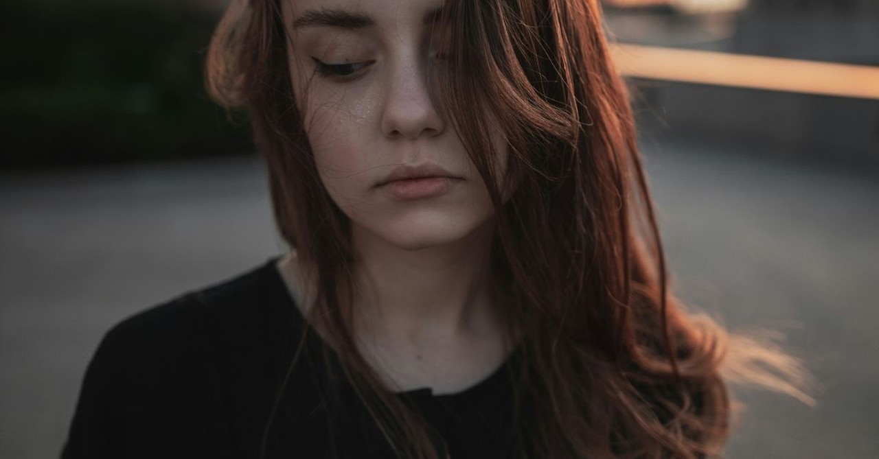 Anxious teen girl with a somber expression, looking down; talk about mental health a lot.