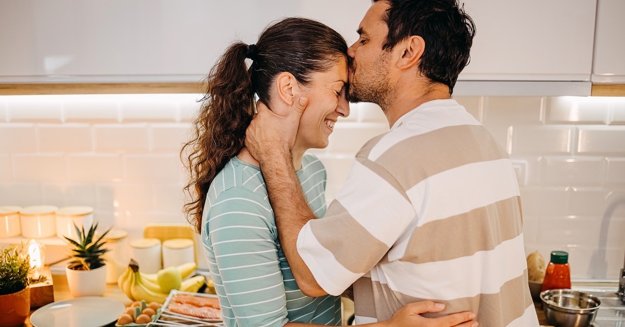 Husband kissing wife on forehead couple in kitchen cooking