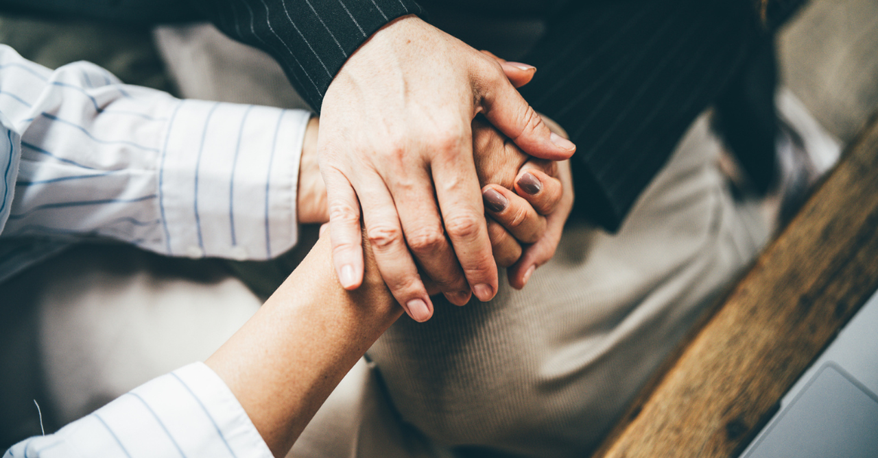 Two middle-aged women hold each other's hands as a sign of support and empathy