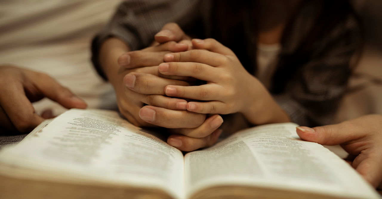 two people holding hands in prayer with a Bible in view