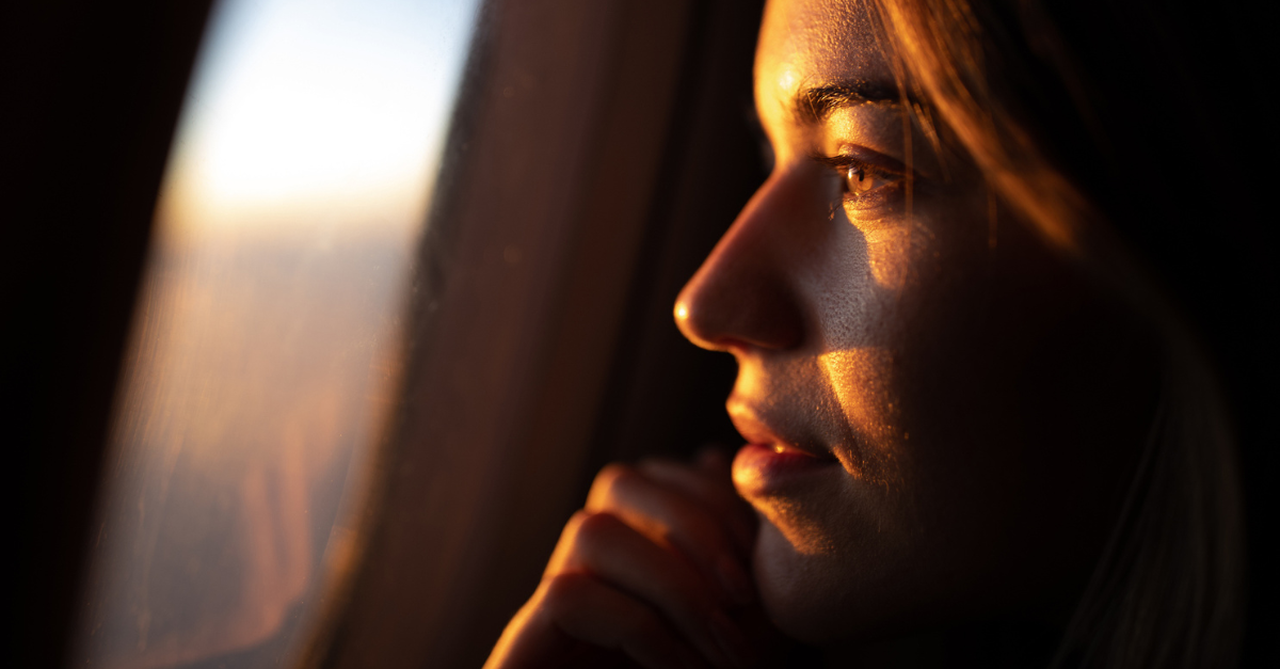 lose up of young woman day dreaming while looking through an airplane window at sunset.