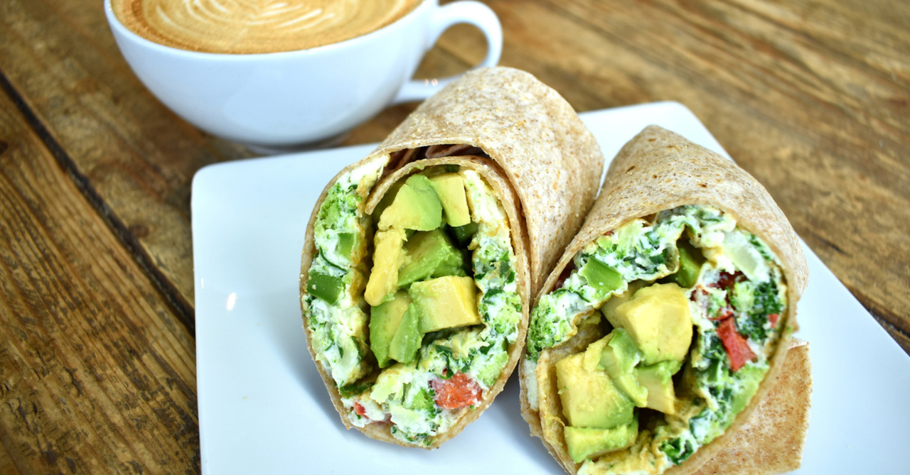 A whole wheat tortilla wrap cut open to show beans, eggs, veggies, and avocado. Bright and appetizing.