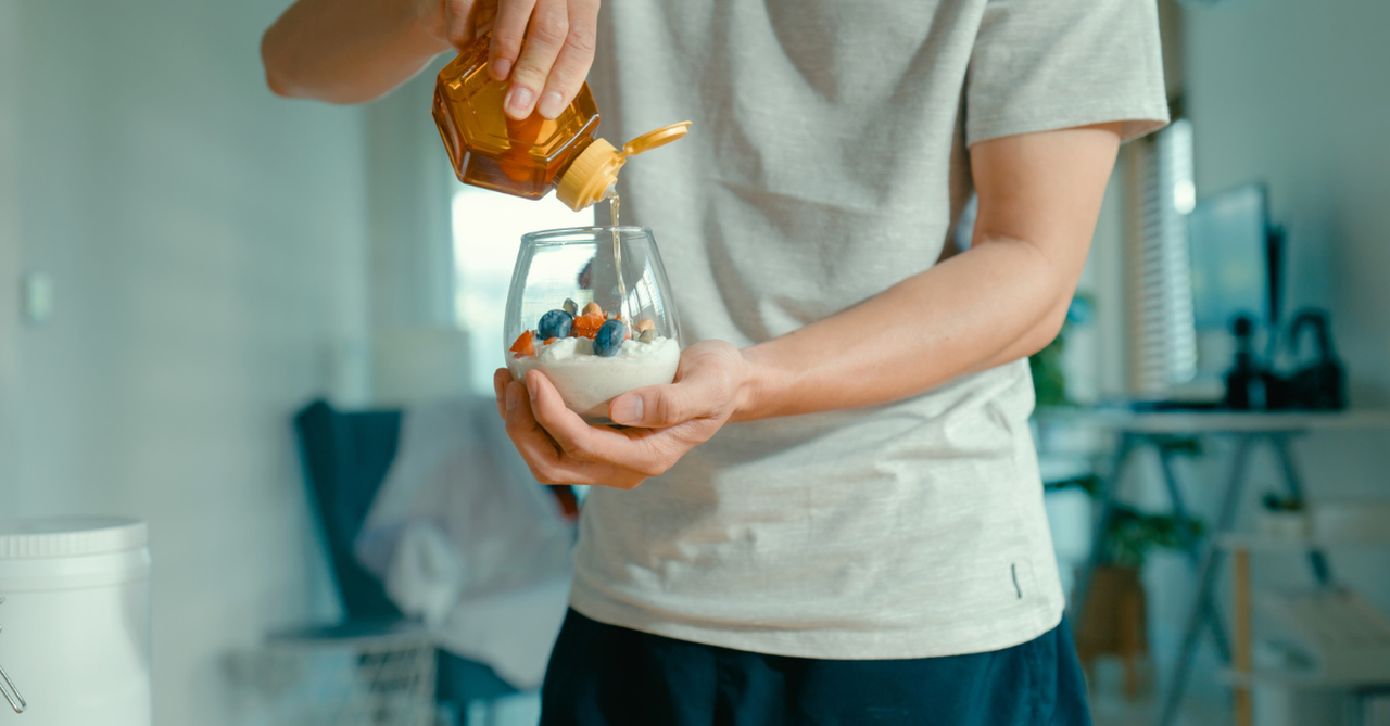 A clear glass layered with yogurt, berries, seeds, and a drizzle of honey.