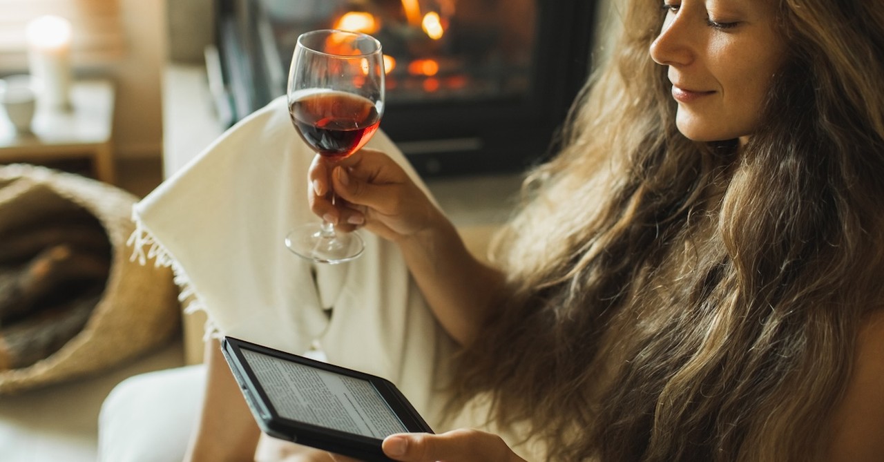 Woman by fire cozy at home drinking wine and reading kindle