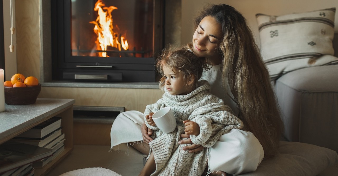 Mother mom and daughter cozy by fire inside winter at home