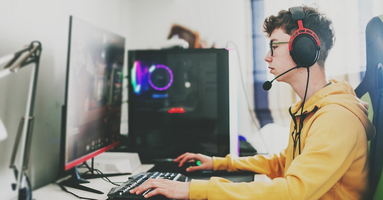 Teen boy gaming on computer headphones video games online laptop