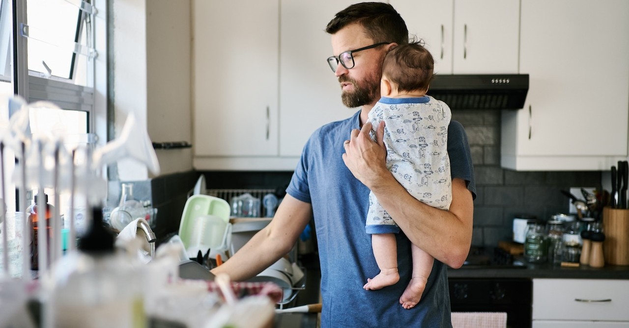 Stressed tired exhausted new dad holding baby and washing dishes