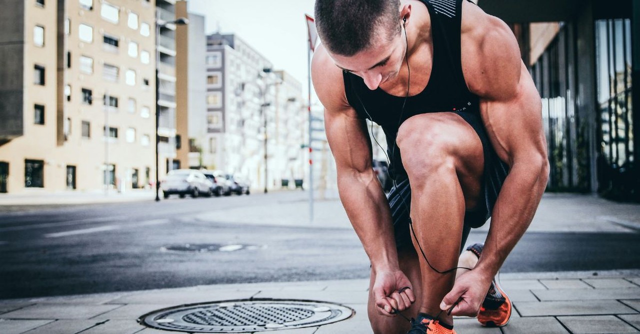 Man tying his running shoe on a city street before a workout