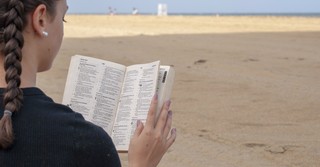 back view of a girl reading the Bible on the beach