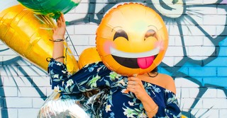 A woman holding a smiley-face emoji balloon over her face