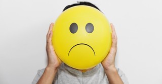 A person holding a balloon with a frowny face in front of their own face