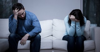 man and woman looking sad and upset sitting on opposite ends of a couch