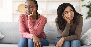 Two women sitting next to each other on a couch, looking unhappy