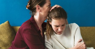 teenage daughter looking distressed and mother hugging