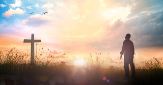 a man standing before a cross at sunrise