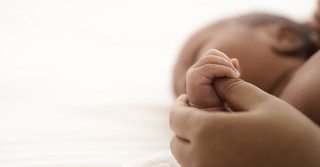 A newborn holding an adult's thumb