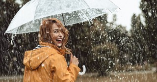 Woman smiling under an umbrella as it rains